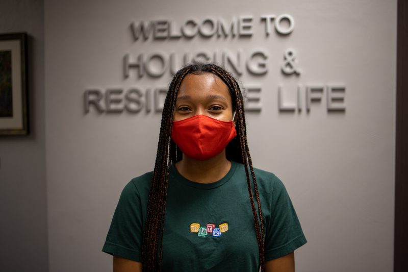 Jorden Piggott (JP) stands in the main entrance to the Housing and Residence Life Office in front of the sign on the wall. Photo by Luke Williams for Virginia Tech.