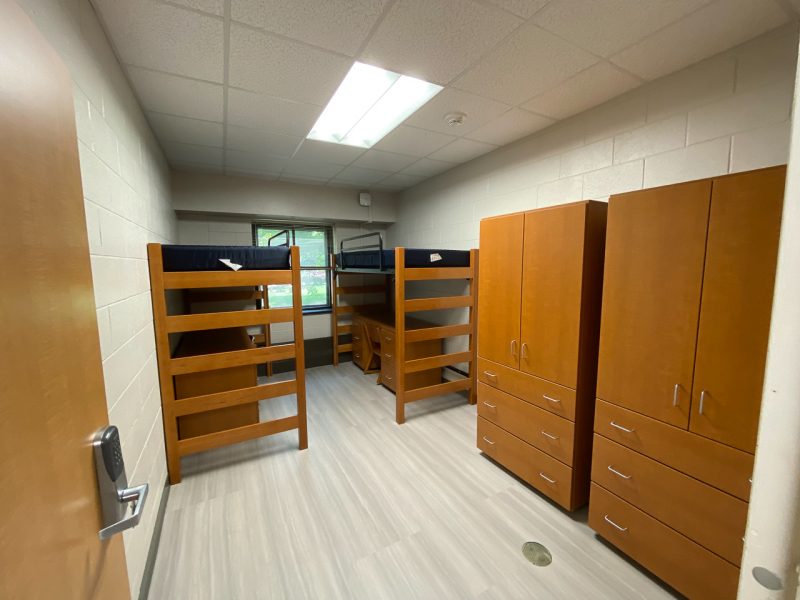 The inside of a traditional-style room in Campbell Hall, with two lofted beds, desks, chairs, wardrobes and a small sink and mirror.