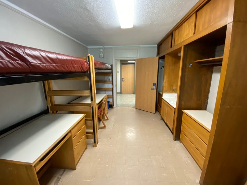 The inside of a traditional-style room in Eggleston Hall, with two lofted beds, desks, chairs, wardrobes and a small sink and mirror.