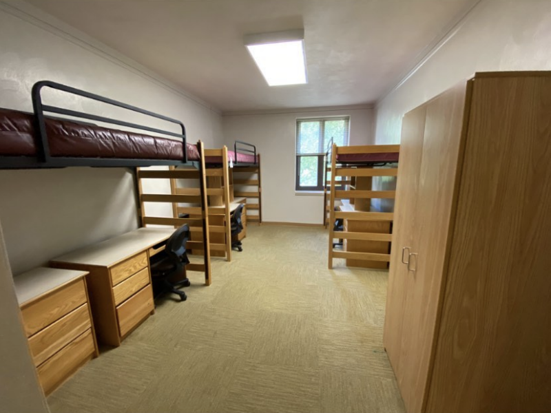 The inside of a private bath-style room in New Hall Suite, with three lofted beds, desks, and chairs.