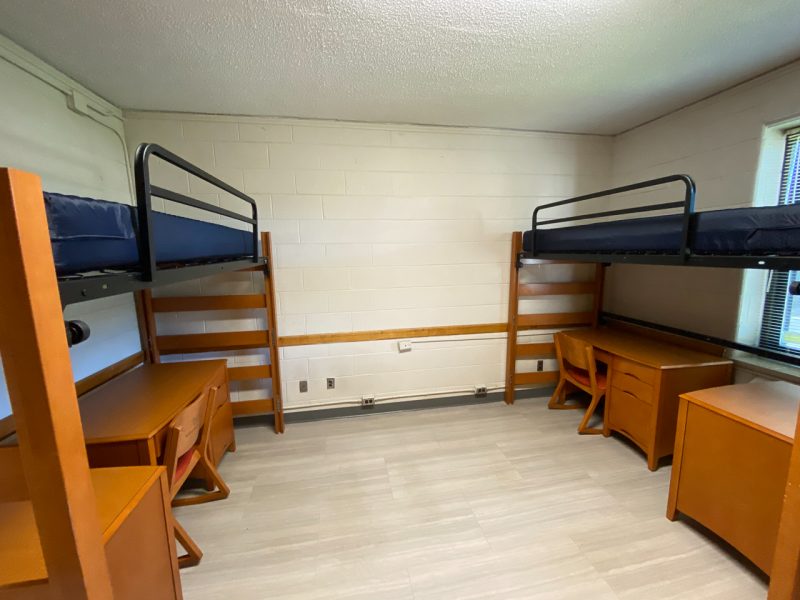 The inside of a traditional-style room in Newman Hall, with two lofted beds, desks, and chairs.
