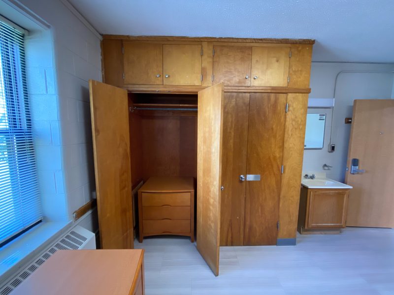 The doors of a built-in closet in Newman Hall are open, revealing a dresser on the floor and a spot to hang clothes.