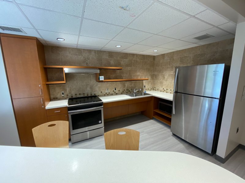 A community kitchen located in Newman Hall, with a fridge, microwave, stove, and counter space.