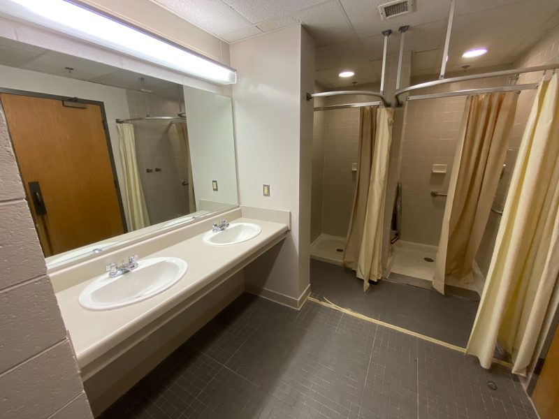 A view into an in-suite bathroom in Payne Hall, showcasing the two sinks, mirror, and two shower stalls with curtains.