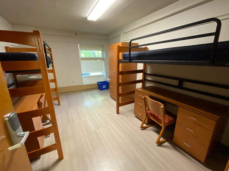 The inside of a traditional-style room in Slusher Hall, with two lofted beds, desks, chairs, clothing storage, and a small sink and mirror.