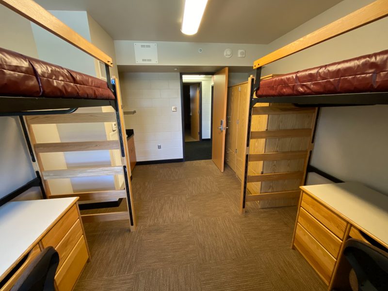 The inside of a traditional-style room in Ambler Johnston, with two lofted beds, desks, chairs, wardrobes and a small sink.