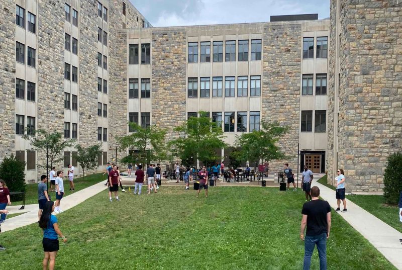 The courtyard at Ambler Johnston, where students socialize on a grassy field underneath trees.