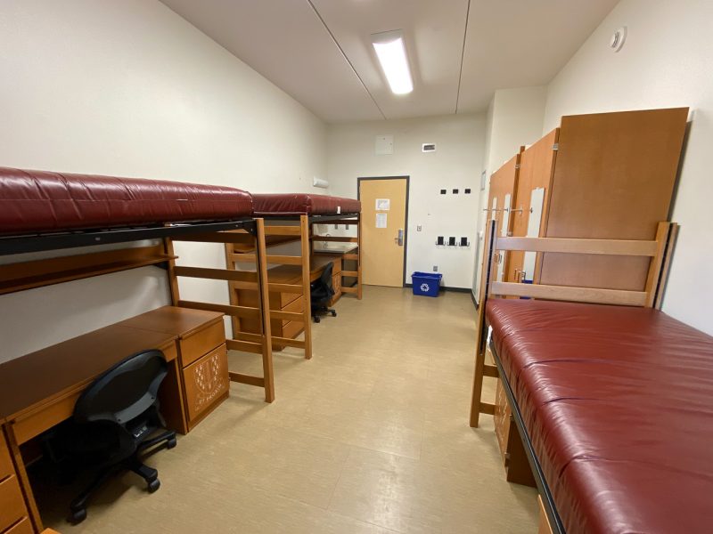 The inside of a traditional-style room in Pearson West, with three lofted beds, desks, chairs, wardrobes and a small sink and mirror.